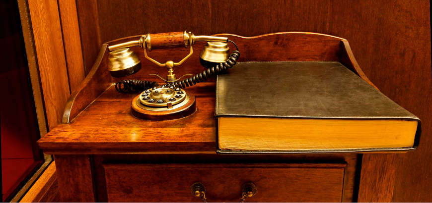 Παλαιό τηλέφωνο και ένα βιβλίο πάνω σε ξύλινο τραπέζι.